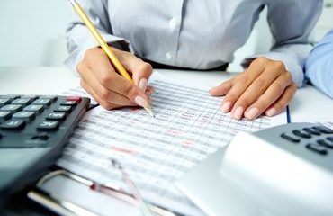 Photo of human hands holding pencil and ticking data in documents